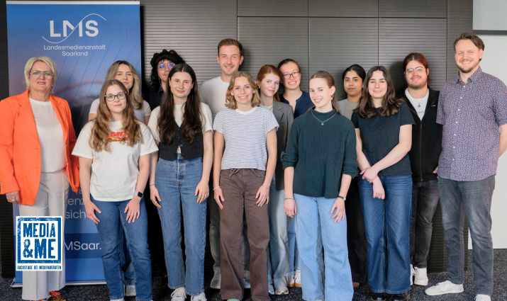 Gruppenfoto der Teilnehmenden und Projektverantwortlichen von Media & Me bei der Landesmedienanstalt Saarland mit LMS-Direktorin Ruth Meyer. Die Gruppe steht vor einem LMS-Banner; unten links ist das Logo von Media & Me eingeblendet.